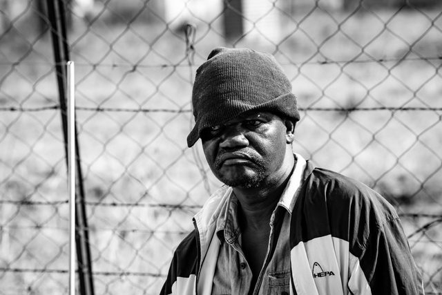 Black and white portrait of a man in a cap in front of a wire fence