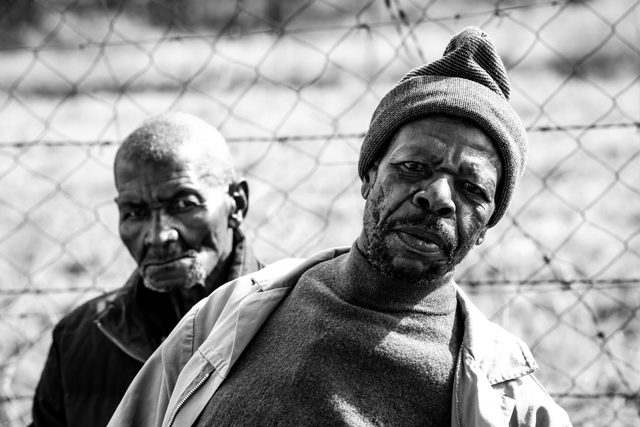 Black and white portrait of two older men in front of a fence