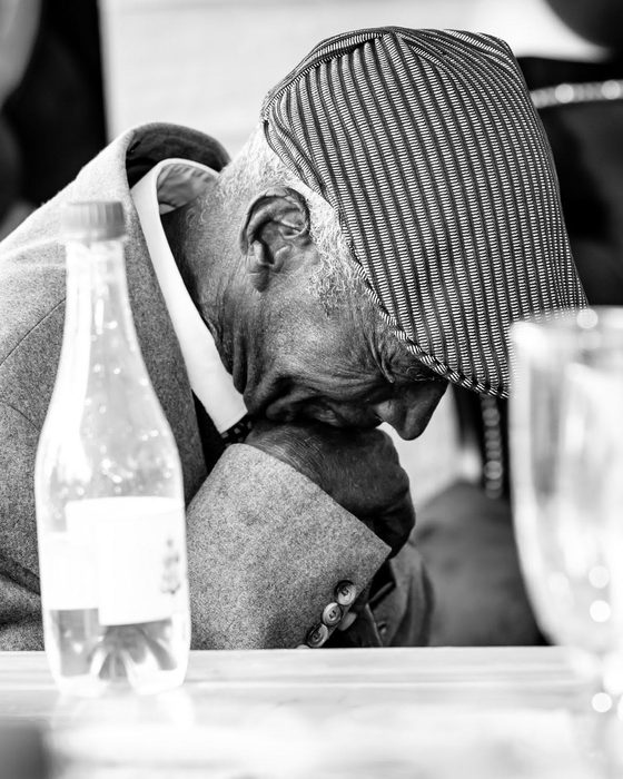 An older man in a striped cap resting his head on his hand at a table
