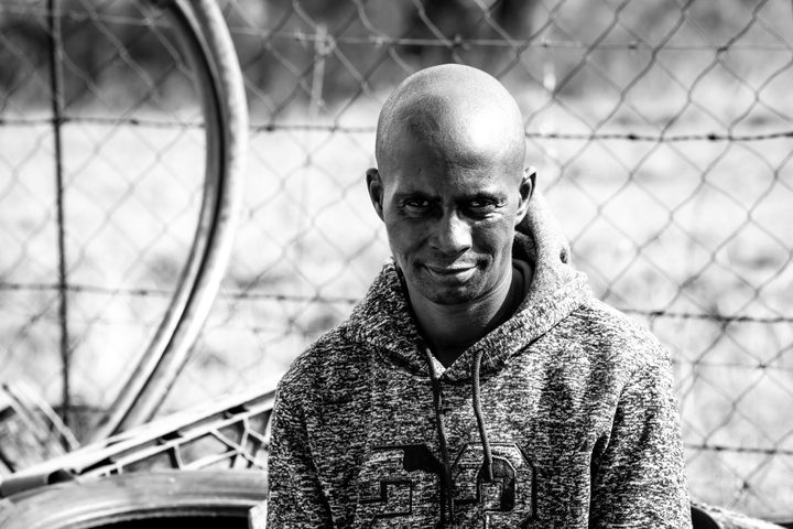 Black and white portrait of a young man in a hoodie in front of a fence